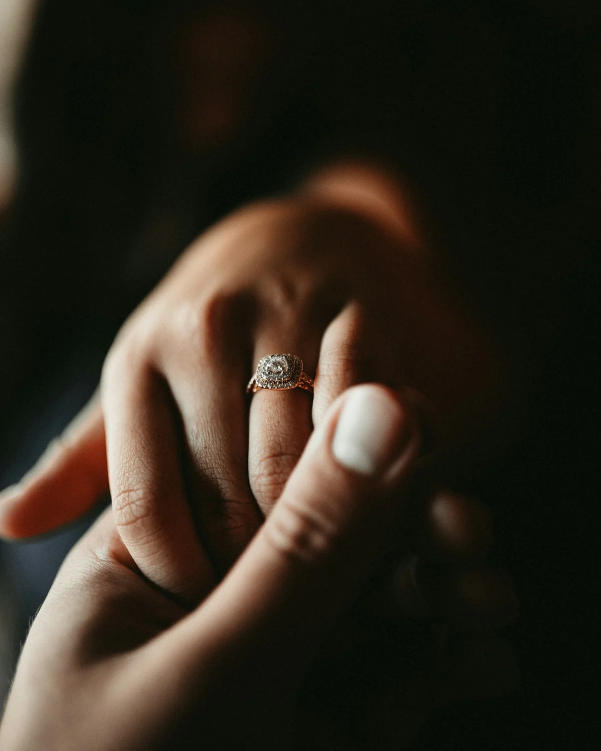 A diamond halo ring being placed on a ring finger.