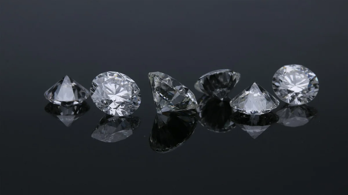 Loose round diamonds photographed on a dark reflective surface.