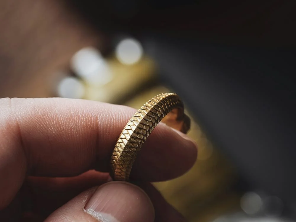 A textured yellow-gold ring held between finger and thumb.
