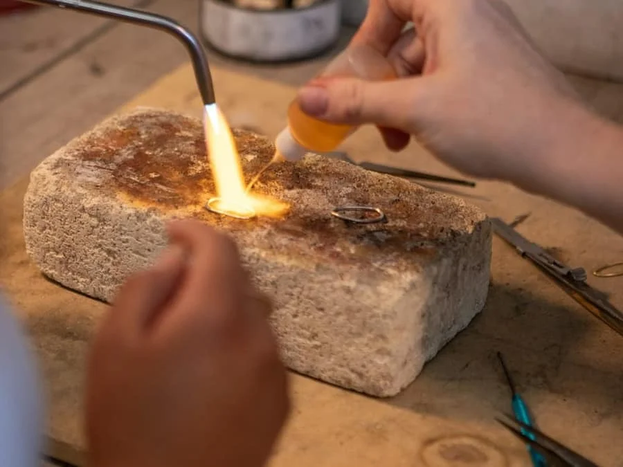 Jeweller’s hands applying a torch to a ring on a soldering block.