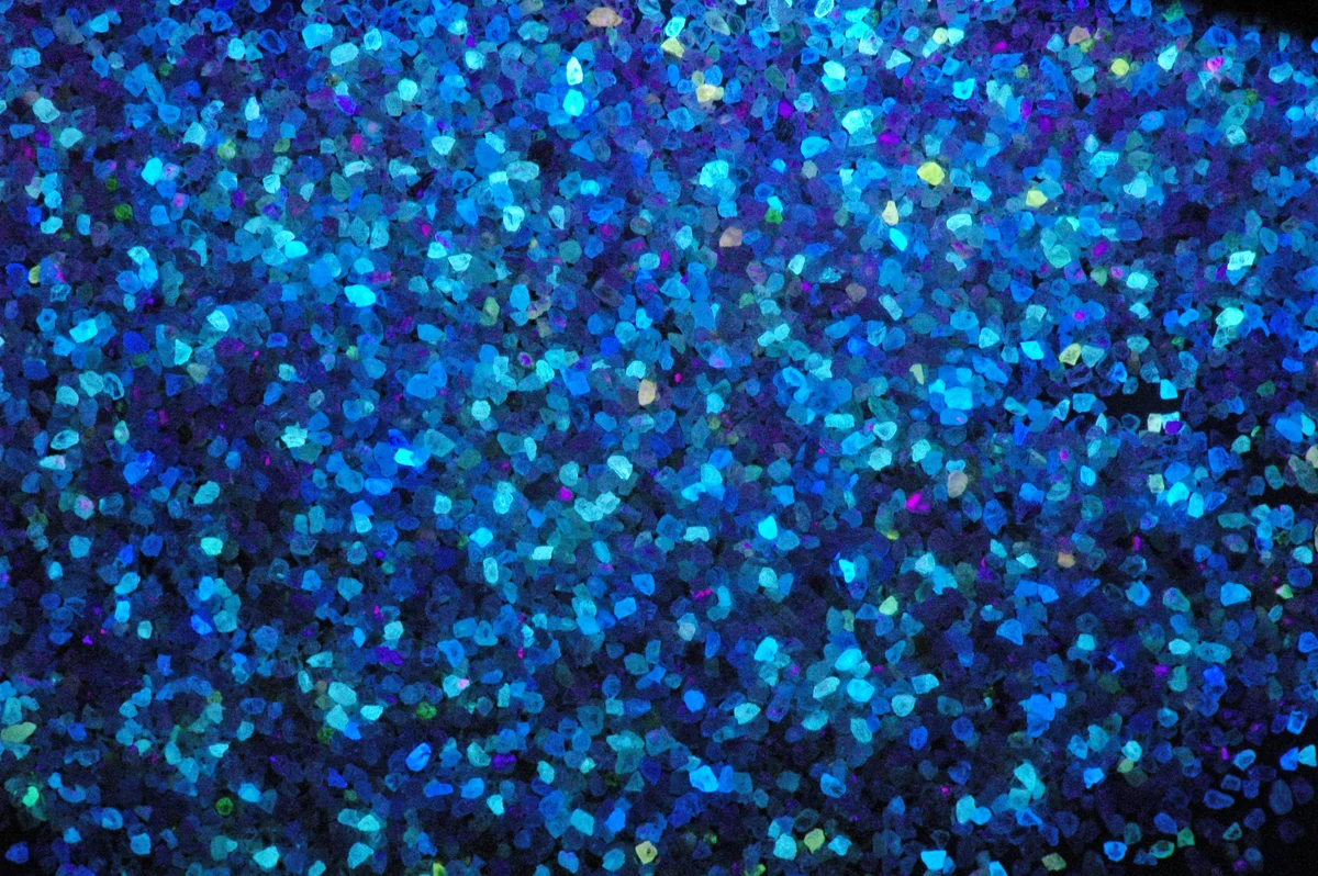 Many tiny diamond crystals glowing blue and other colours under ultraviolet light.