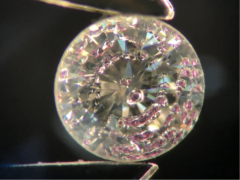 Magnified polished diamond with a purple crystal inclusion and its reflections.