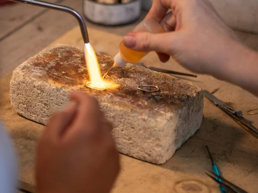 A jeweller's torch flame heating a gold ring on a soldering block