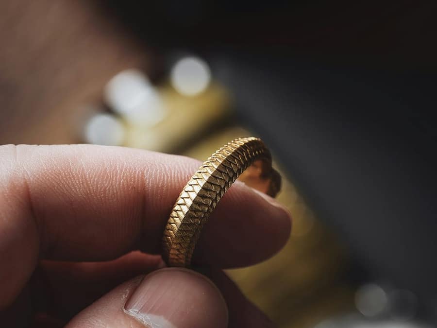 Fingers holding a textured gold band up to the light