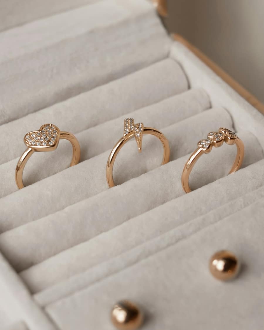 Three fine rose-gold rings seated in the cream velvet slots of a jewellery case